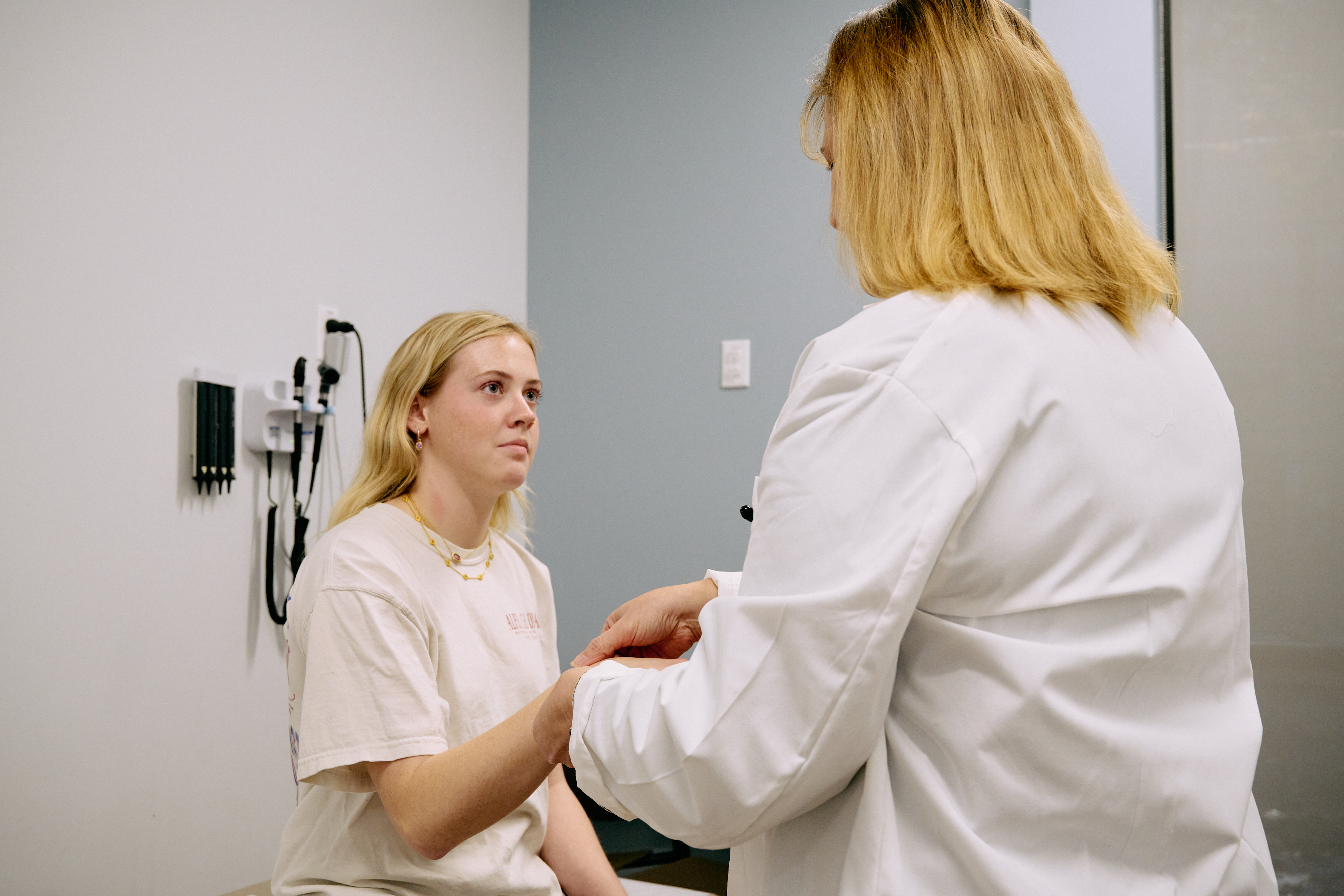 A healthcare provider in a white coat holds a patient's hand while listening during a primary care visit at SHSU Physicians.