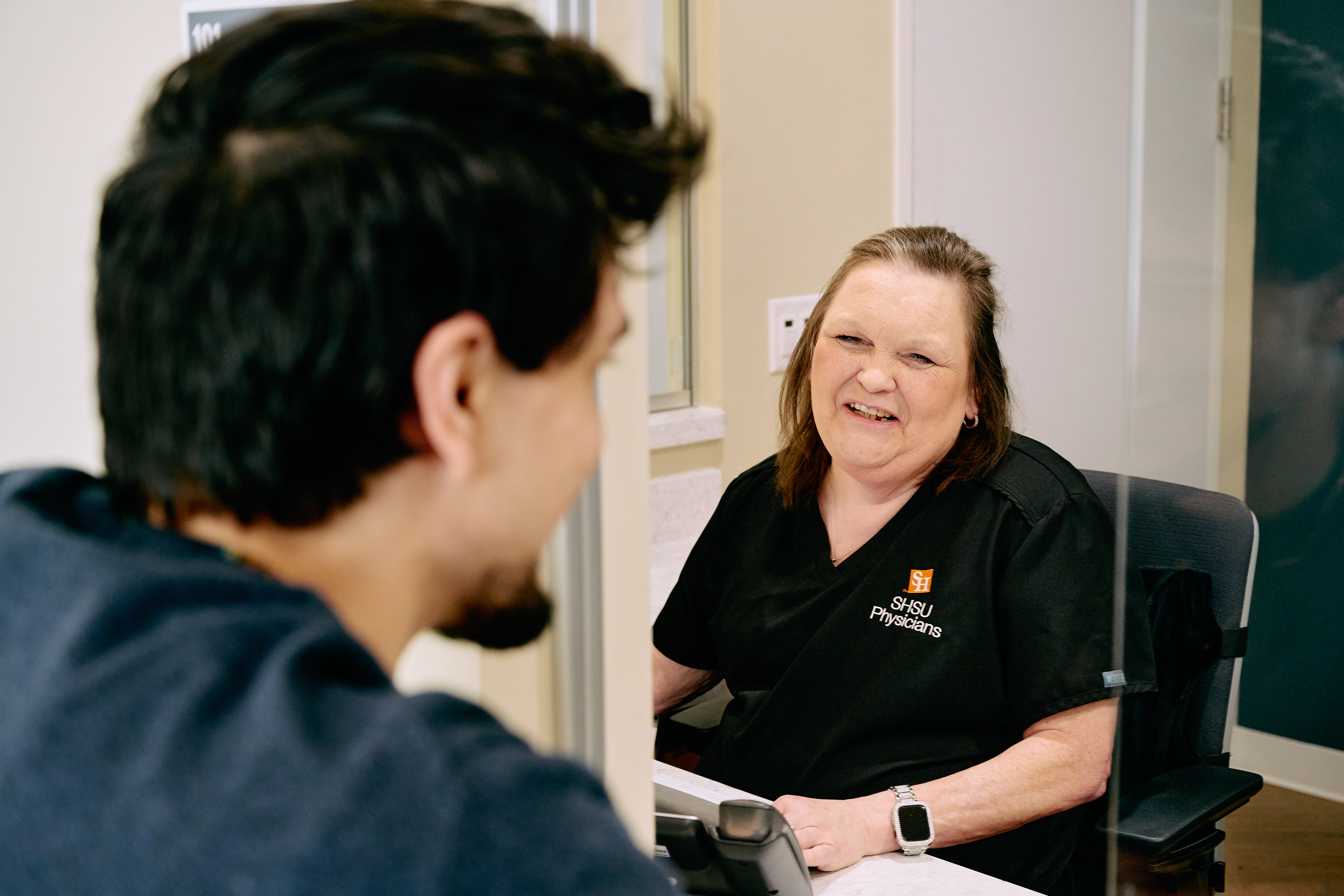 SHSU Physicians staff member greets a patient at the front desk with a friendly smile during check-in.